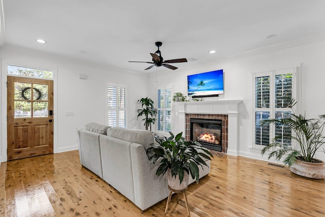 living area featuring light wood finished floors, baseboards, a tiled fireplace, crown molding, and recessed lighting