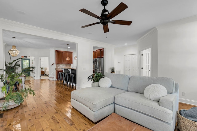 living area featuring ornamental molding, light wood-type flooring, a ceiling fan, and baseboards