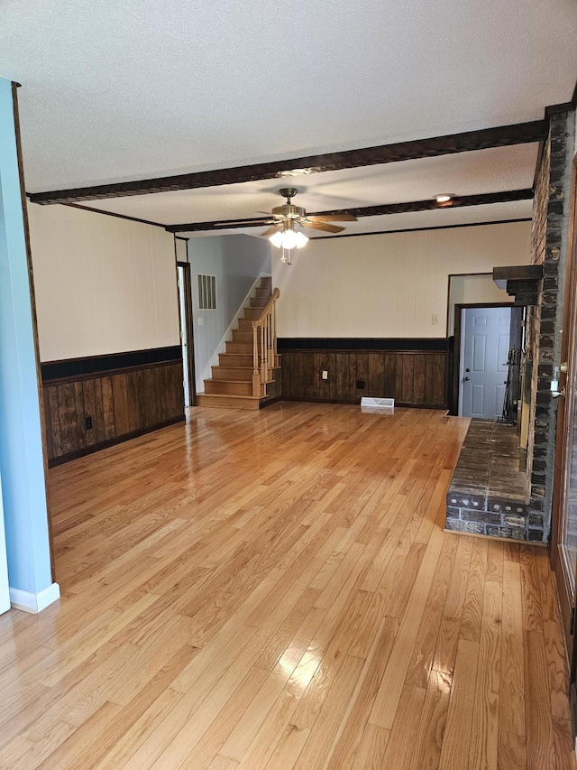 101 Brittany Ct, Summerville, SC 29485 - unfurnished living room with wooden walls, light wood finished floors, a wainscoted wall, beamed ceiling, and a ceiling fan