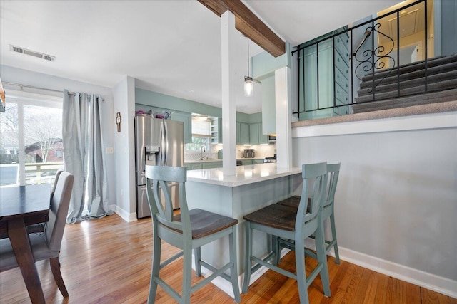 dining room featuring light wood finished floors, visible vents, baseboards, and beam ceiling