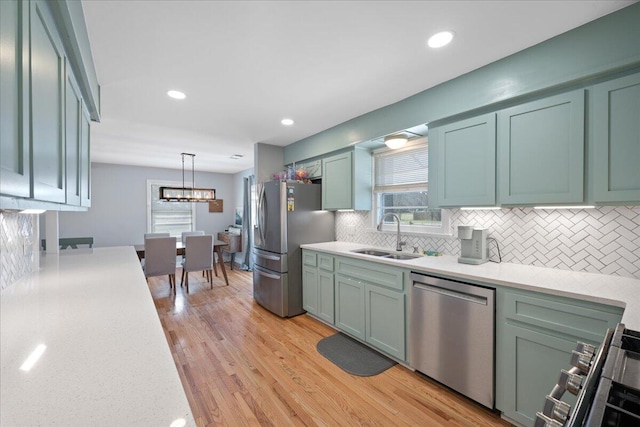 kitchen featuring a sink, backsplash, stainless steel appliances, light wood finished floors, and hanging light fixtures