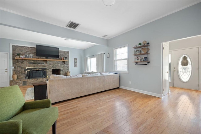 living room featuring visible vents, a brick fireplace, baseboards, ornamental molding, and light wood-style flooring