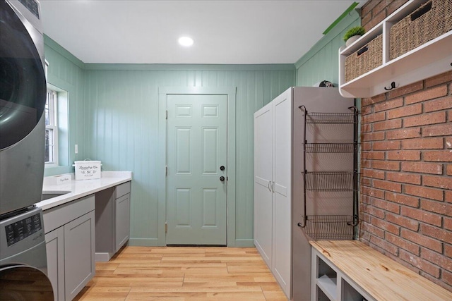 laundry room featuring cabinet space, light wood-style flooring, and stacked washer and dryer