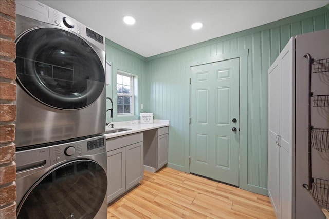 laundry room with stacked washing maching and dryer, recessed lighting, cabinet space, a sink, and light wood-style floors