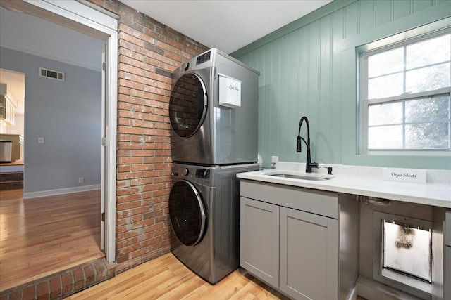 clothes washing area with visible vents, stacked washer and dryer, a sink, cabinet space, and light wood-style floors