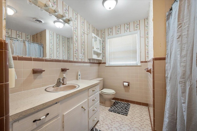 bathroom featuring tile patterned flooring, wallpapered walls, toilet, wainscoting, and tile walls