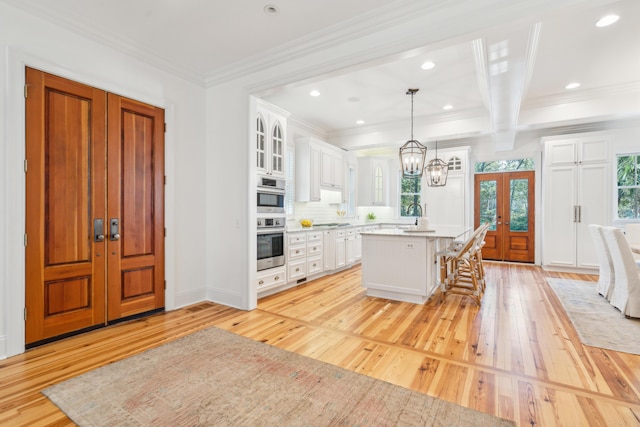 kitchen featuring white cabinets, a kitchen island, decorative light fixtures, a kitchen bar, and french doors