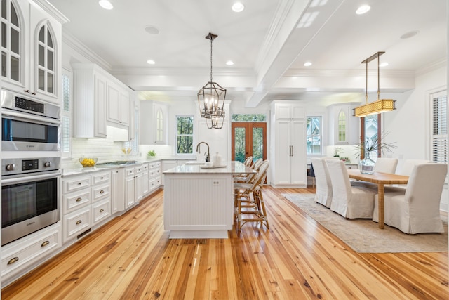 kitchen with decorative light fixtures, white cabinets, a kitchen island with sink, and light hardwood / wood-style flooring