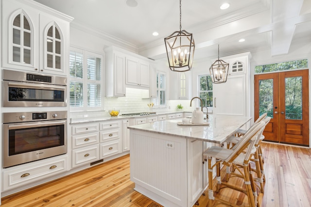 kitchen featuring hanging light fixtures, a kitchen island with sink, appliances with stainless steel finishes, light stone countertops, and french doors