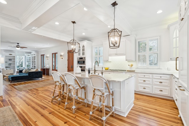 kitchen featuring decorative backsplash, white cabinetry, a kitchen breakfast bar, an island with sink, and ceiling fan with notable chandelier