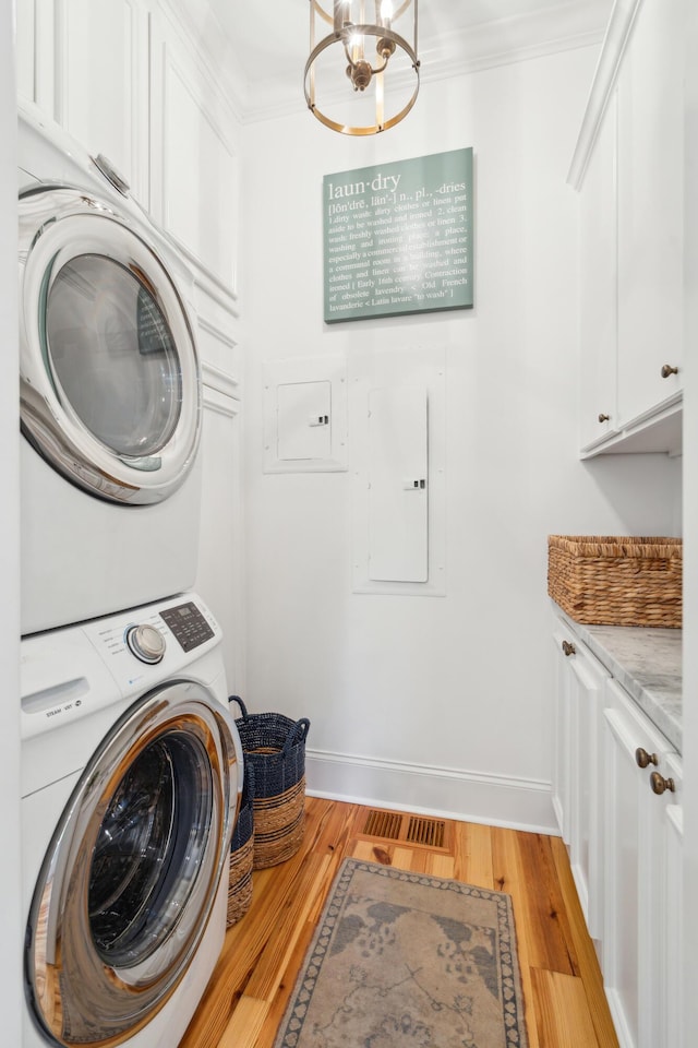 laundry room with stacked washer and clothes dryer, light wood-type flooring, cabinets, electric panel, and crown molding