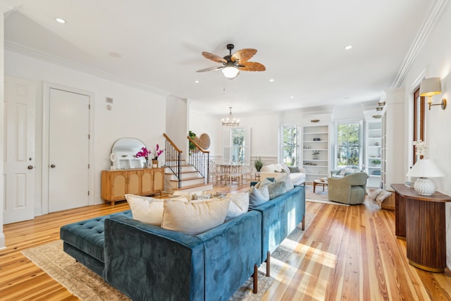 living room featuring built in shelves, ceiling fan with notable chandelier, ornamental molding, and light hardwood / wood-style flooring