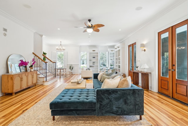 living room with ceiling fan with notable chandelier, built in shelves, french doors, light hardwood / wood-style flooring, and crown molding