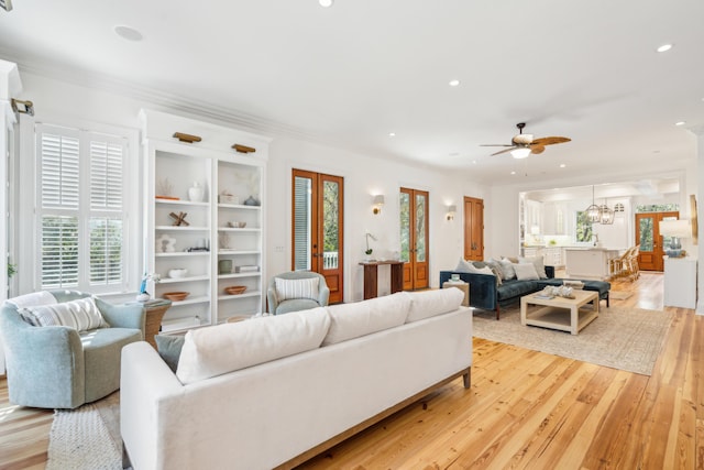 living room featuring light hardwood / wood-style floors, ornamental molding, and ceiling fan with notable chandelier