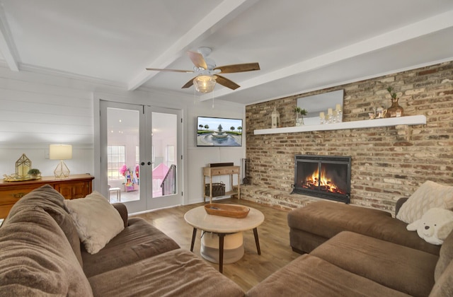 living room with light hardwood / wood-style floors, ceiling fan, a brick fireplace, beam ceiling, and french doors