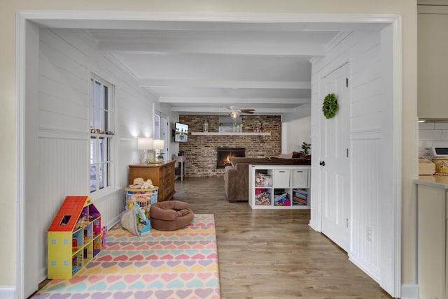 playroom with beamed ceiling, ceiling fan, wood-type flooring, and a fireplace