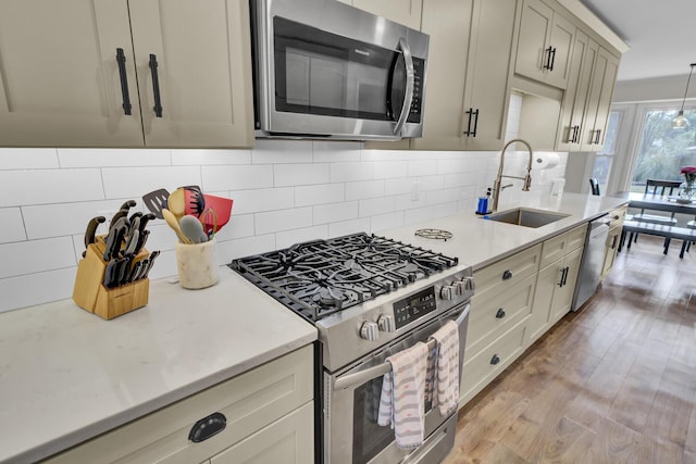 kitchen featuring sink, hanging light fixtures, backsplash, stainless steel appliances, and light hardwood / wood-style floors