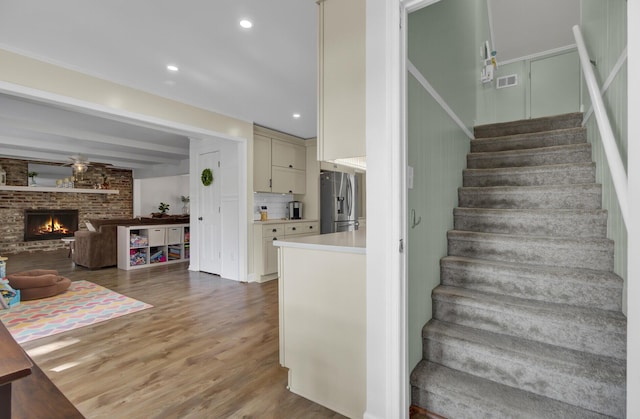 stairs featuring a brick fireplace, hardwood / wood-style flooring, and ceiling fan