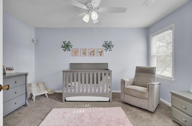 carpeted bedroom with ceiling fan and a crib