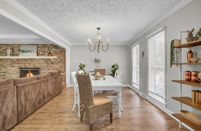 dining room featuring crown molding, a brick fireplace, a chandelier, and light hardwood / wood-style flooring