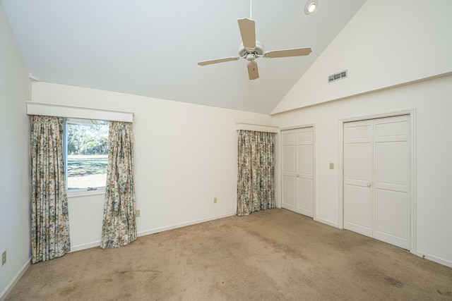 unfurnished bedroom featuring ceiling fan, light carpet, high vaulted ceiling, and multiple closets