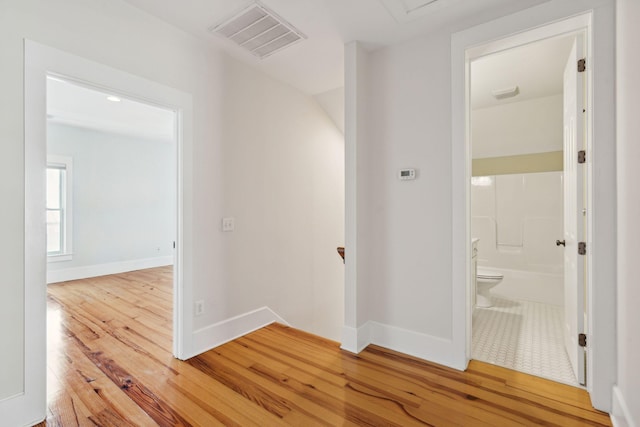 hallway with visible vents, baseboards, an upstairs landing, and light wood-style floors