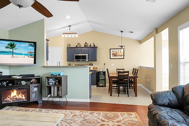 interior space with visible vents, a glass covered fireplace, wood finished floors, a ceiling fan, and vaulted ceiling