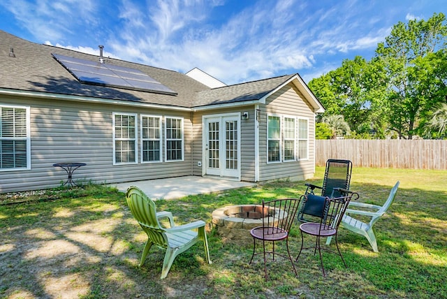 back of house featuring fence, roof mounted solar panels, a patio area, a lawn, and a fire pit