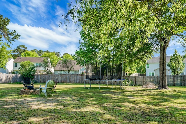 view of yard featuring a fenced backyard, a trampoline, an outdoor fire pit, and a residential view