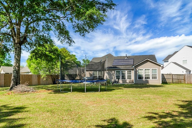 back of property featuring a trampoline, a yard, and solar panels