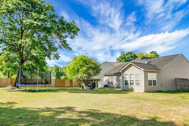 rear view of property featuring a lawn, a fenced backyard, and a trampoline