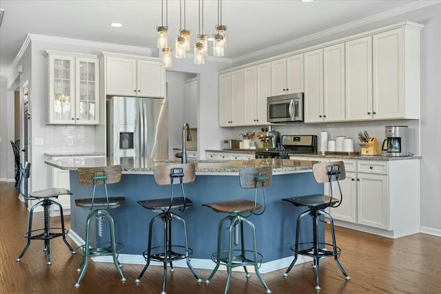 kitchen with appliances with stainless steel finishes, a breakfast bar, white cabinetry, decorative backsplash, and a center island with sink