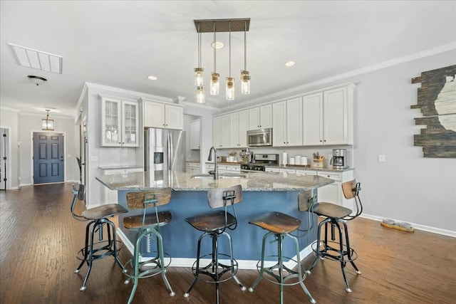 kitchen with white cabinetry, stainless steel appliances, a kitchen breakfast bar, and an island with sink