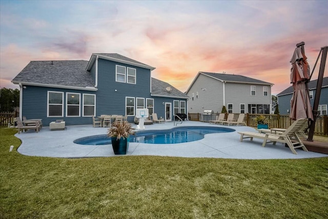 back house at dusk featuring a lawn and a patio