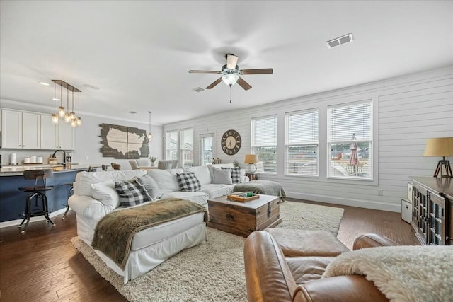 living room featuring crown molding, dark wood-type flooring, ceiling fan, and wood walls