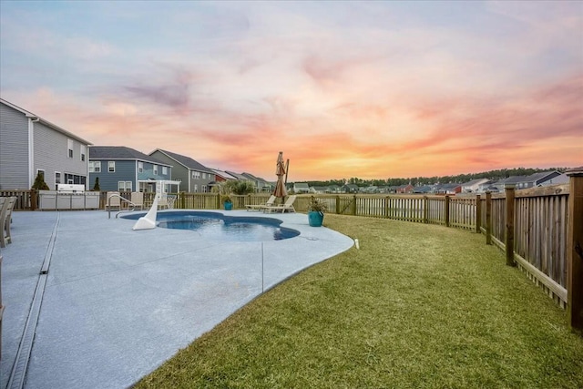 pool at dusk featuring a patio area and a lawn