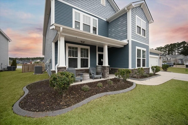 view of front facade with a garage, central AC unit, covered porch, and a lawn