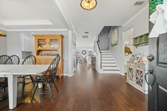 dining room with a raised ceiling, ornamental molding, and dark wood-type flooring