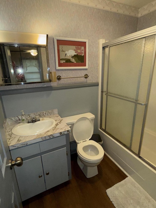 full bathroom with hardwood / wood-style flooring, bath / shower combo with glass door, vanity, and toilet