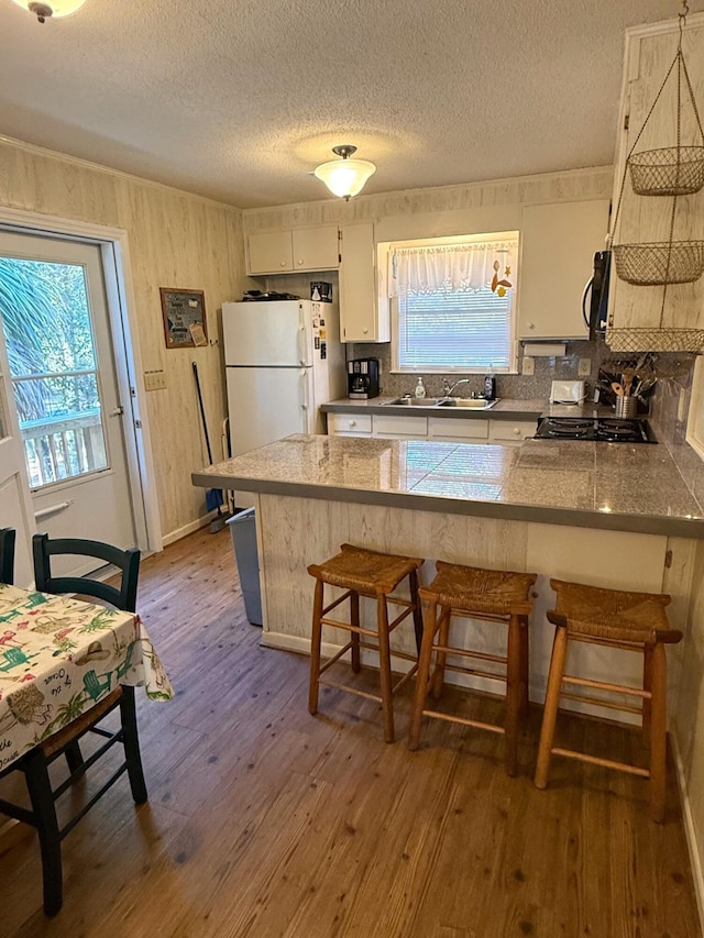 kitchen with sink, a kitchen bar, light wood-type flooring, kitchen peninsula, and white fridge