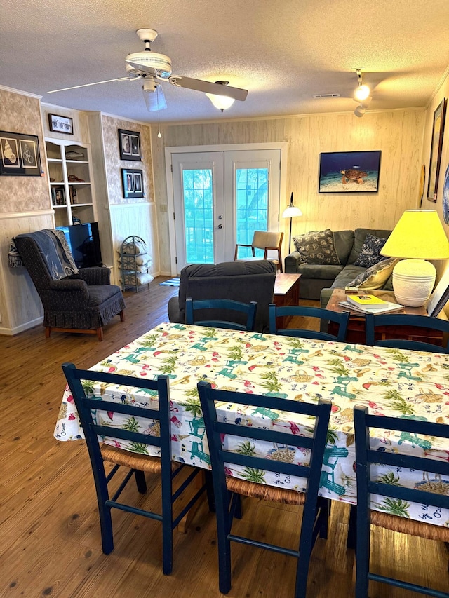 dining room featuring hardwood / wood-style flooring, ceiling fan, a textured ceiling, french doors, and wood walls