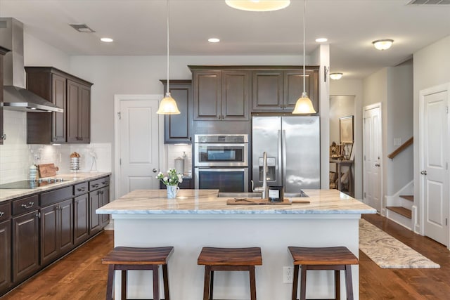 kitchen featuring a center island with sink, dark wood-type flooring, wall chimney range hood, and stainless steel appliances