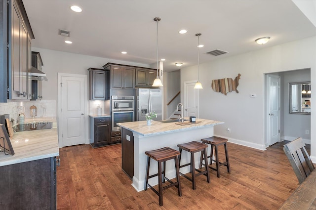 kitchen featuring decorative light fixtures, stainless steel appliances, a center island with sink, and dark hardwood / wood-style flooring