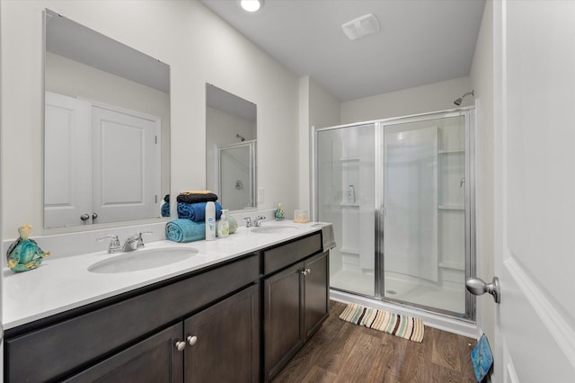 full bath featuring a shower stall, wood finished floors, double vanity, and a sink