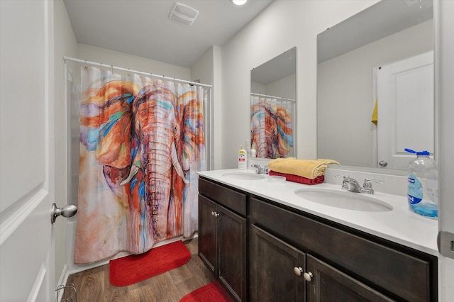 bathroom with a sink, visible vents, wood finished floors, and double vanity