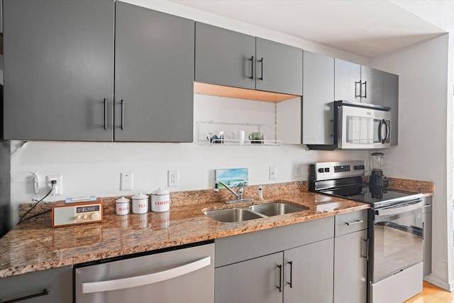 kitchen with light stone counters, a sink, gray cabinets, and appliances with stainless steel finishes