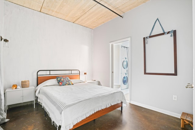 bedroom with baseboards, connected bathroom, concrete flooring, and stacked washer / dryer