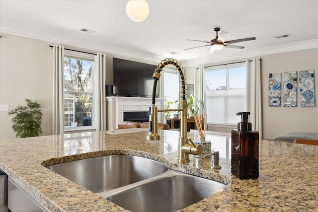 kitchen with a sink, a fireplace, visible vents, and ornamental molding