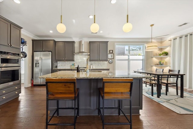 kitchen featuring light stone countertops, stainless steel appliances, crown molding, wall chimney exhaust hood, and tasteful backsplash