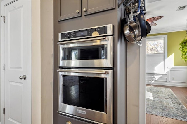 kitchen featuring visible vents, gray cabinetry, wood finished floors, stainless steel double oven, and crown molding